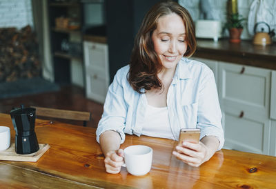 Mid adult woman holding coffee cup on table at home