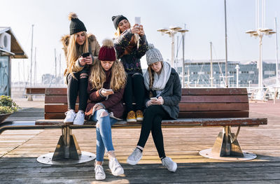 Four young women sitting on a bench using their cell phones