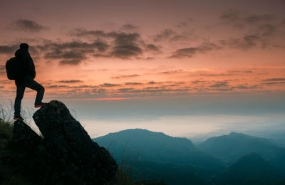Man standing on rock against sky during sunset