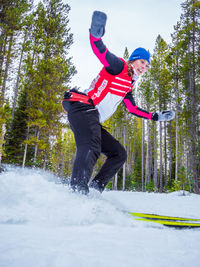 Low angle view of woman jumping on snow against trees