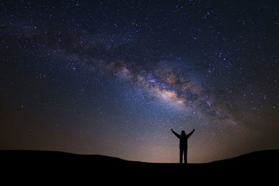 Silhouette man with arms raised standing against star field at night