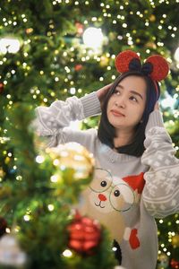 Portrait of smiling young woman standing against christmas tree