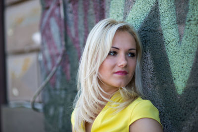 Close-up of thoughtful young woman looking away while standing by wall