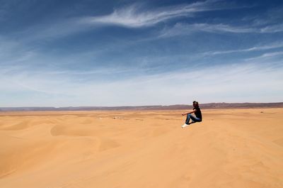 Full length of woman sitting on sand dune at sahara desert against sky