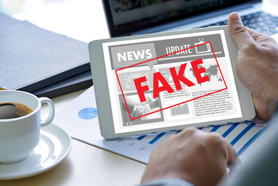 Cropped hand holding fake news in digital tablet