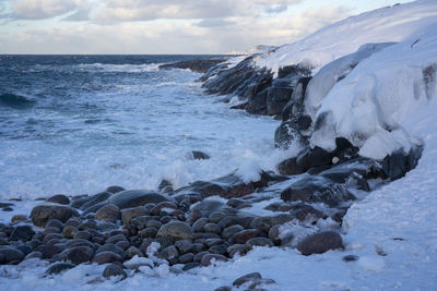 Waves splashing on rocks at shore against sky