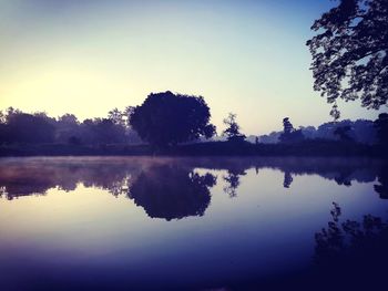 Reflection of silhouette trees in lake against clear sky