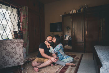 Woman kissing man while sitting on carpet in living room at home