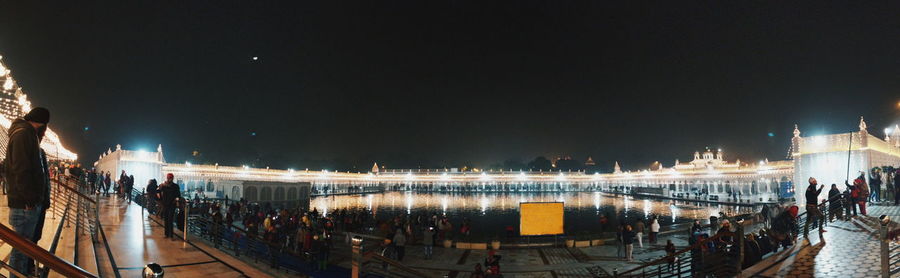 People on illuminated city against sky at night