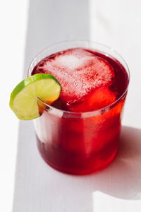 Agua de jamaica, hibiscus tea drink with ice in rocks glass, lime wheel garnish, white background