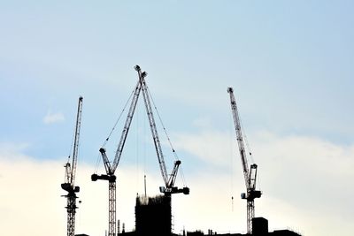 Low angle view of cranes at construction site against sky