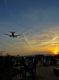 Airplane flying at airport against sky during sunset