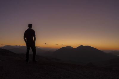 Rear view of silhouette man standing on mountain against sunset sky