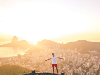 Full length of man standing on city against sky during sunset