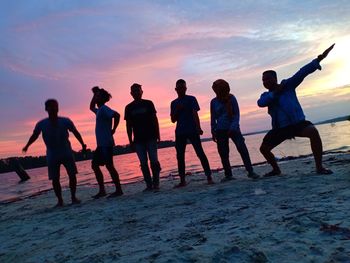 Silhouette people on beach against sky during sunset