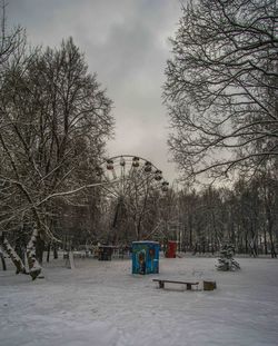 Bare trees on snow covered field against sky