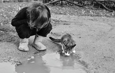 Boy crouching by kitten at puddle