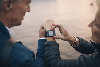 Cropped image of senior woman showing time to man on smart watch