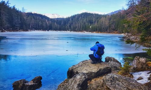 Rear view of woman on rocks by lake against blue sky