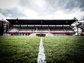 Grassy field at stadium against cloudy sky