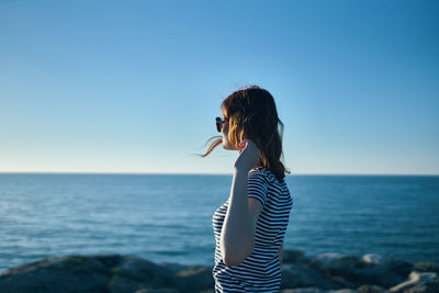 Side view of young woman standing in sea against clear sky