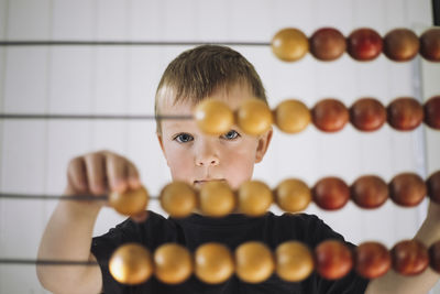 Portrait of schoolboy using abacus to count in classroom at kindergarten