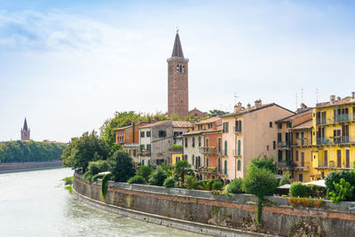 Canal by bell tower in city against sky