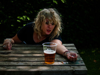 Woman drinking beer while holding pills on table