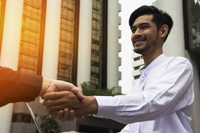 Businessmen shaking hands while standing against office buildings