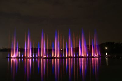 Illuminated fountain at lake against sky at night