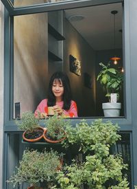 Portrait of young woman standing by potted plant