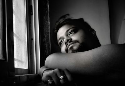 Close-up of thoughtful young man looking through window while sitting at home