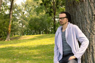 Pensive man leaning on a tree while relaxing in nature in spring day.