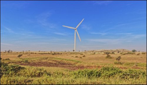 Wind turbines on field against blue sky