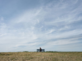 Woman sitting on bench against sky