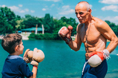Shirtless grandfather with grandson boxing by swimming pool
