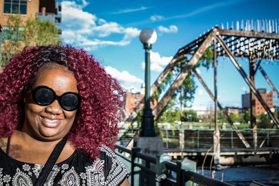 Portrait of woman with curly maroon hair while wearing sunglasses in city