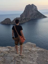 Rear view of woman standing on rock against sky