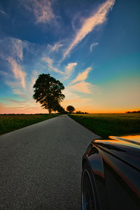 Road by trees against sky during sunset