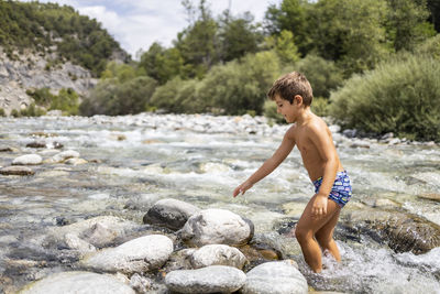 Side view of shirtless boy on rock