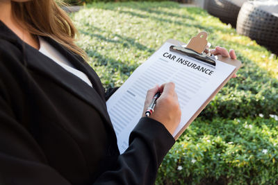 Midsection of female agent with car insurance documents in yard