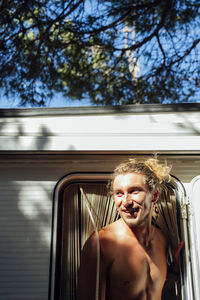 Smiling shirtless man with blond hair standing at doorway of camper van