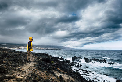 Side view of man standing at beach against cloudy sky