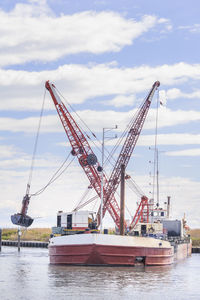 Cranes at harbor against sky