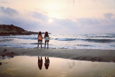 Friends standing on beach against sky during sunset