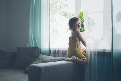 Child jumps and plays on sofa in minimalist living room, gray sofa.