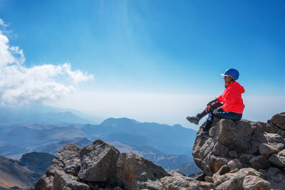 Side view of woman sitting on mountain cliff