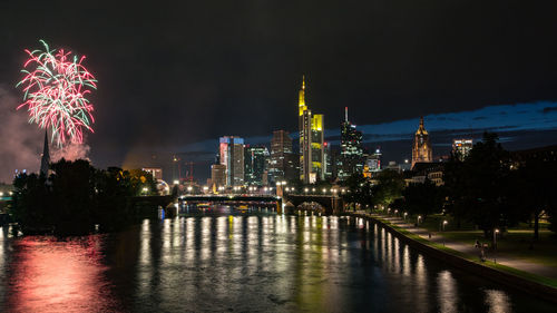 Firework display over river and illuminated buildings in city at night