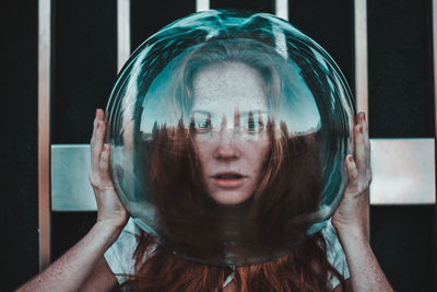 Close-up portrait of young woman wearing glass helmet in head against metallic railing