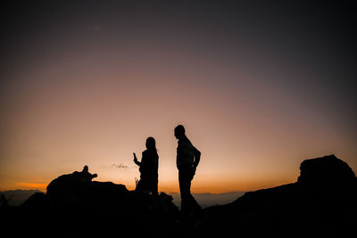 Silhouette people standing on rock against sky during sunset
